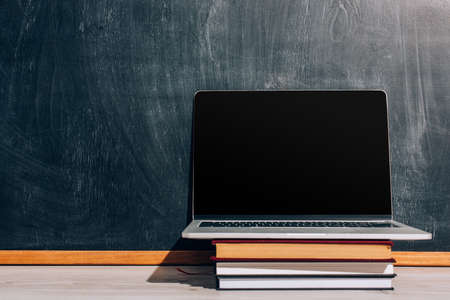 laptop with with blank screen on stack of textbooks near black chalkboardの写真素材