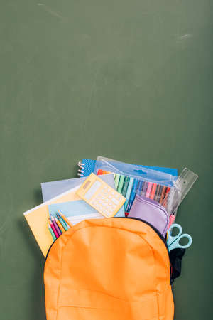 top view of backpack packed with school stationery on green chalkboardの写真素材