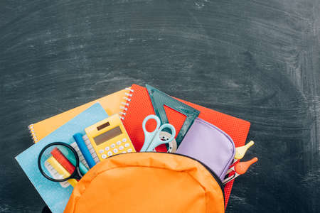 top view of backpack with school supplies on black chalkboardの写真素材