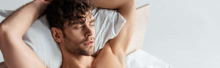 Horizontal image of handsome shirtless man lying on bed isolated on whiteの写真素材