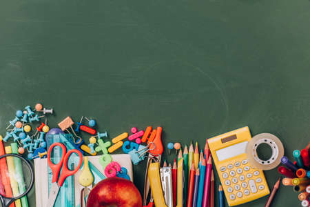 top view of apple, calculator and school supplies on green chalkboardの写真素材