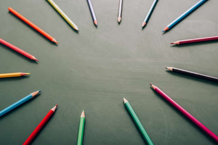 selective focus of circle frame of color pencils on green chalkboard, high angle view