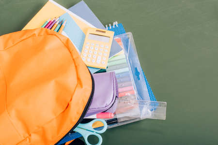 high angle view of yellow backpack with school supplies on green chalkboard