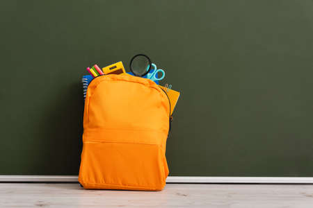 yellow backpack full of school stationery on desk near green chalkboard