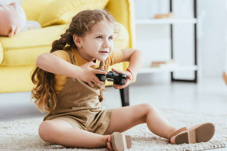 KYIV, UKRAINE - JUNE 19, 2020: adorable, focused child playing video game while sitting on floorの写真素材