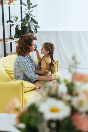 selective focus of adorable kid sitting on laps of young nanny while looking at each otherの写真素材