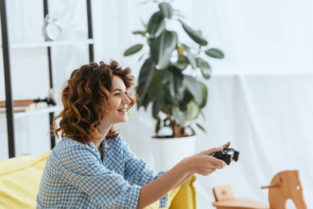 KYIV, UKRAINE - JUNE 19, 2020: side view of happy woman playing video game with gamepadの写真素材