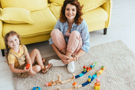 high angle view of happy nurse and child looking at camera while sitting on floor near carton box and multicolored blocksの写真素材