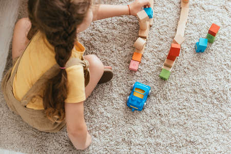 top view of child sitting on floor and playing with multicolored blocks