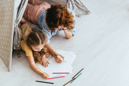 high angle view of nanny and child drawing while lying in toy wigwamの写真素材