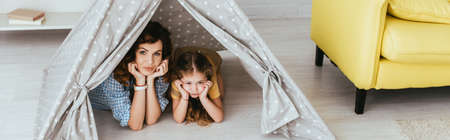 horizontal image of nanny and kid looking at camera while lying in toy wigwamの写真素材