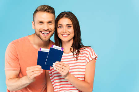 happy couple holding passports with air tickets isolated on blueの写真素材