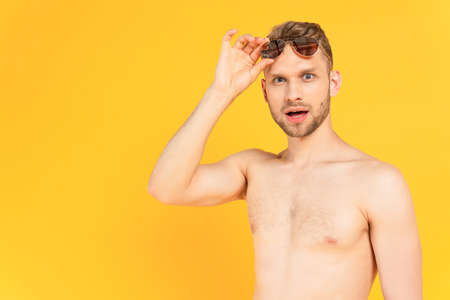 shocked and shirtless man touching sunglasses isolated on yellowの写真素材