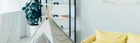 toy wigwam near green potted plant and rack in living room, panoramic shotの写真素材