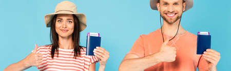 panoramic shot of happy man and woman in hats holding passports and showing thumbs up isolated on...