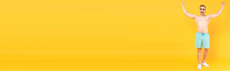 panoramic concept of excited and shirtless man in sunglasses standing with hands above head on yellowの写真素材