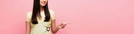 panoramic crop of cheerful girl pointing with finger isolated on pinkの写真素材
