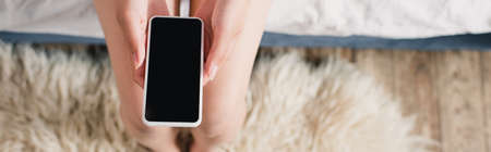 Panoramic shot of woman holding smartphone with blank screen on bed