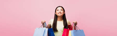 horizontal image of cheerful young asian woman looking up while holding shopping bags isolated on...