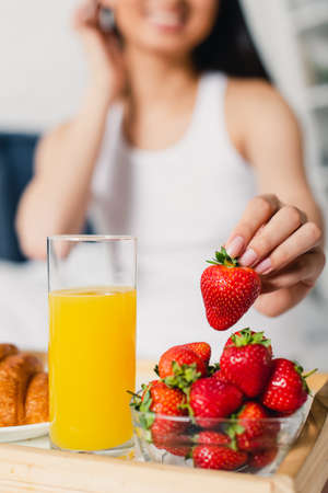 Selective focus of woman taking fresh strawberry near glass of orange juice and growing on breakfast...