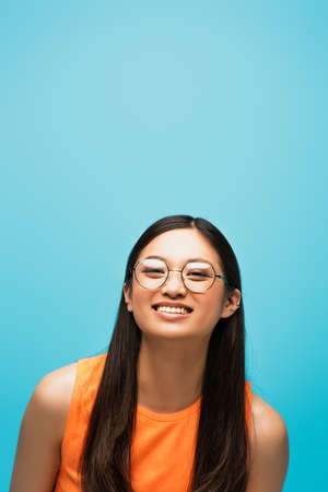 cheerful asian girl in glasses smiling isolated on blue