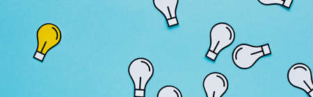 panoramic shot of paper light bulbs scattered on blue background, business concept
