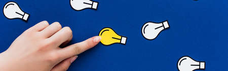 cropped view of hand pointing at paper light bulb on blue background, business concept