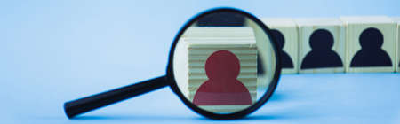 selective focus of magnifying glass near wooden block with red human icon on blue background, leadership concept, panoramic shotの写真素材