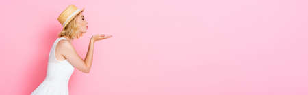 side view of woman straw hat and dress sending air kiss on pink, panoramic cropの写真素材