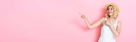 horizontal image of woman in white dress and straw hat pointing with fingers on pinkの写真素材