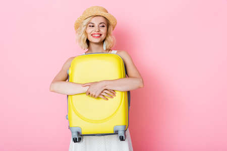 woman in straw hat hugging yellow luggage on pinkの写真素材