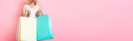 horizontal crop of surprised woman in white dress holding shopping bags on pink