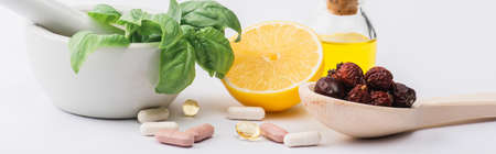 green leaves in mortar, berries and lemon near pills on white background, naturopathy conceptの写真素材