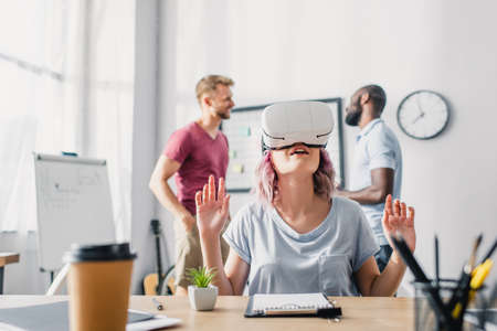 Selective focus of businesswoman using vr headset while multicultural businessmen talking in officeの写真素材