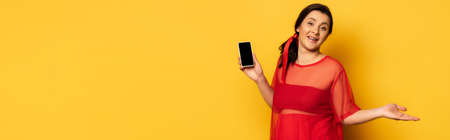 pregnant woman in red outfit holding smartphone with blank screen on yellow, website header