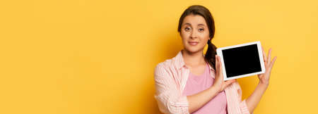 horizontal image of young woman showing digital tablet with blank screen on yellow
