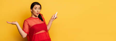 horizontal image of confused pregnant woman showing shrug gesture while holding pregnancy test on yellowの写真素材