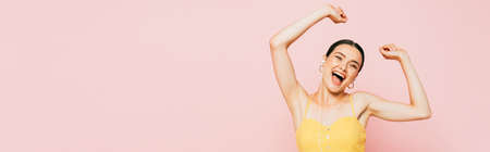 excited brunette young woman in earphones dancing isolated on pink, panoramic shot