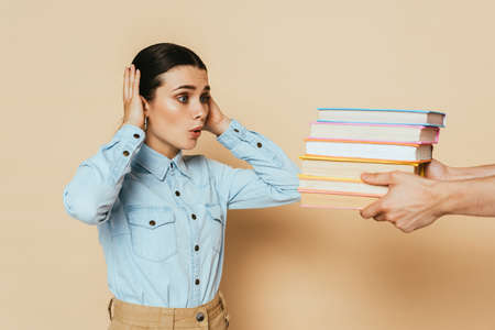 shocked student in denim shirt looking at books on beigeの写真素材