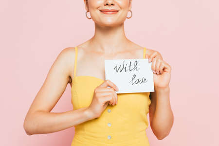 cropped view of young woman holding with love card isolated on pinkの写真素材