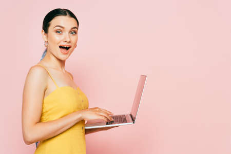 side view of shocked brunette young woman using laptop on pinkの写真素材