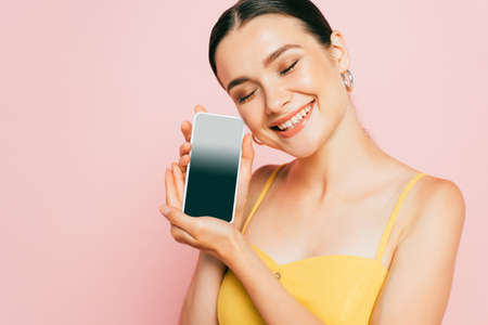 brunette young woman holding smartphone with blank screen isolated on pinkの写真素材