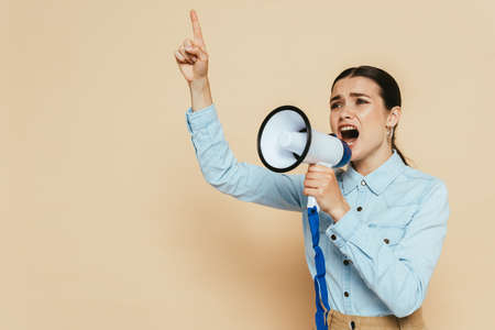brunette woman in denim shirt screaming in loudspeaker on beigeの写真素材