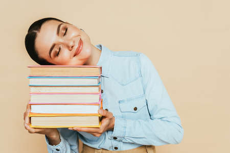 pleased student in denim shirt with books isolated on beigeの写真素材