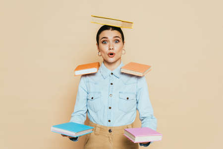 shocked student in denim shirt with books on body isolated on beigeの写真素材