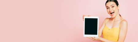 excited brunette young woman presenting digital tablet with blank screen isolated on pink, panoramic...
