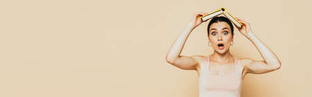 shocked brunette young woman with book on head on beige, panoramic shotの写真素材