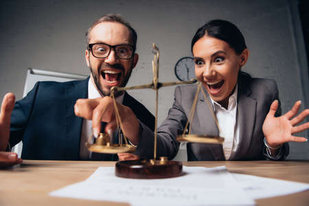 selective focus of bearded businessman and excited businesswoman in formal wear touching scalesの写真素材