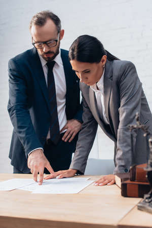 selective focus of bearded lawyer pointing with finger at document near businesswoman in officeの写真素材