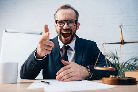 selective focus of excited and bearded lawyer pointing with finger near scalesの写真素材